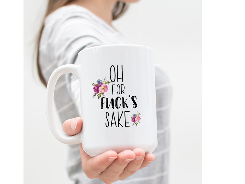 K&ouml;nnte beinhalten: Wei&szlig;e Keramik-Kaffeetasse mit schwarzem Blumendesign und dem Text "OH FOR FUCK'S SAKE".