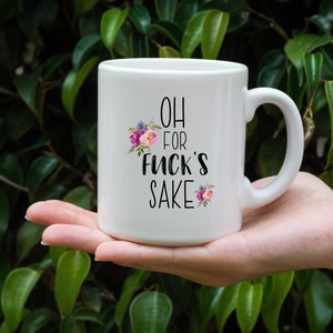 K&ouml;nnte beinhalten: Wei&szlig;e Keramik-Kaffeetasse mit schwarzem Blumendesign und dem Text "OH FOR FUCK'S SAKE".
