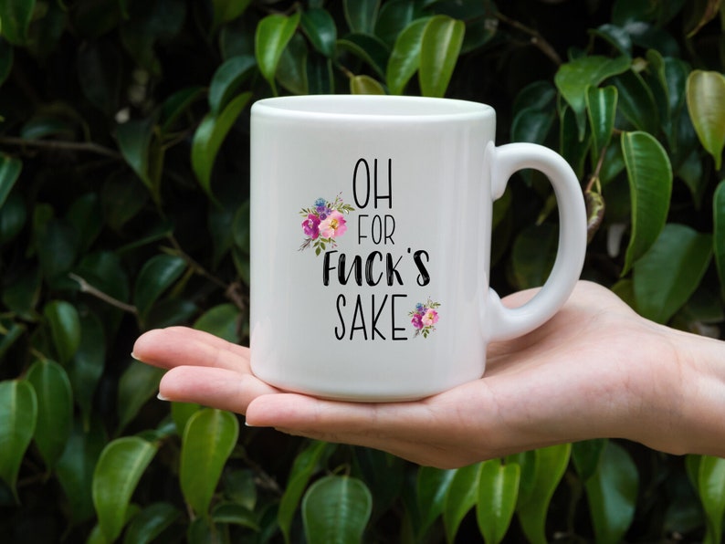 K&ouml;nnte beinhalten: Wei&szlig;e Keramik-Kaffeetasse mit schwarzem Blumendesign und dem Text "OH FOR FUCK'S SAKE".