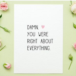 Puede incluir: Una tarjeta blanca con el texto "DAMN. YOU WERE RIGHT ABOUT EVERYTHING." y un s&iacute;mbolo de coraz&oacute;n rosa. La tarjeta est&aacute; rodeada de rosas rosas y capullos sobre un fondo verde claro.