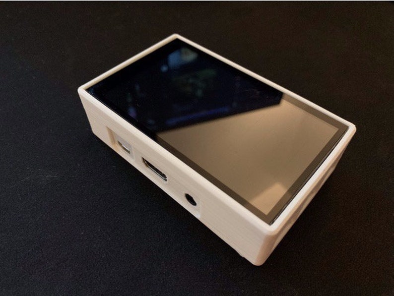 May include: A rectangular, cream-coloured electronic device with a black screen. The device has a sleek design with a black border around the screen. It features ports on the side, including a USB port and a headphone jack.