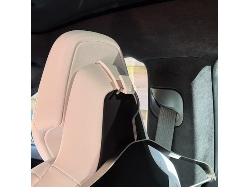 May include: Close-up of a car seat headrest. The headrest is a light cream color with black accents. A seatbelt is visible to the right. The interior of the car is dark.