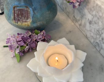 May include: White ceramic candle holder shaped like a flower with a small tea light candle burning inside.