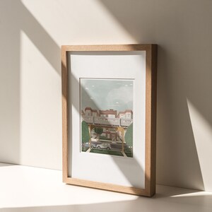 May include: A framed illustration of a city street with a train track overhead. The buildings are red brick and the street is lined with trees. There are two cars parked on the street and a person walking.