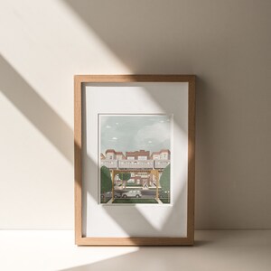 May include: A framed illustration of a city street scene with a building in the background and a car driving down the street. The illustration is in a light brown frame.