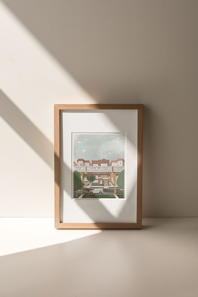 May include: A framed illustration of a city street scene with a building in the background and a car driving down the street. The illustration is in a light brown frame.