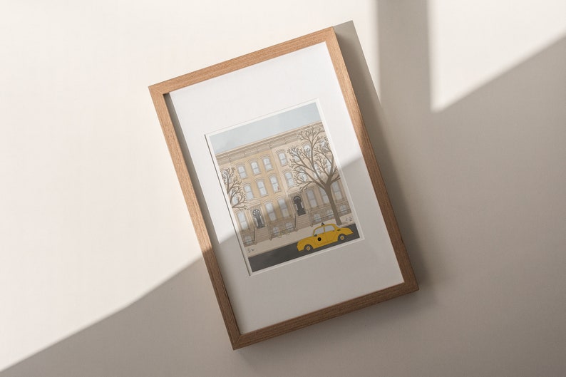 May include: A framed illustration of a yellow taxi cab parked in front of a row of brownstone buildings with trees in the foreground.