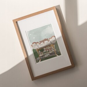 May include: A framed illustration of a street scene with a row of houses, a car, and people walking. The houses are painted in shades of brown and white, with green trees and a blue sky in the background.