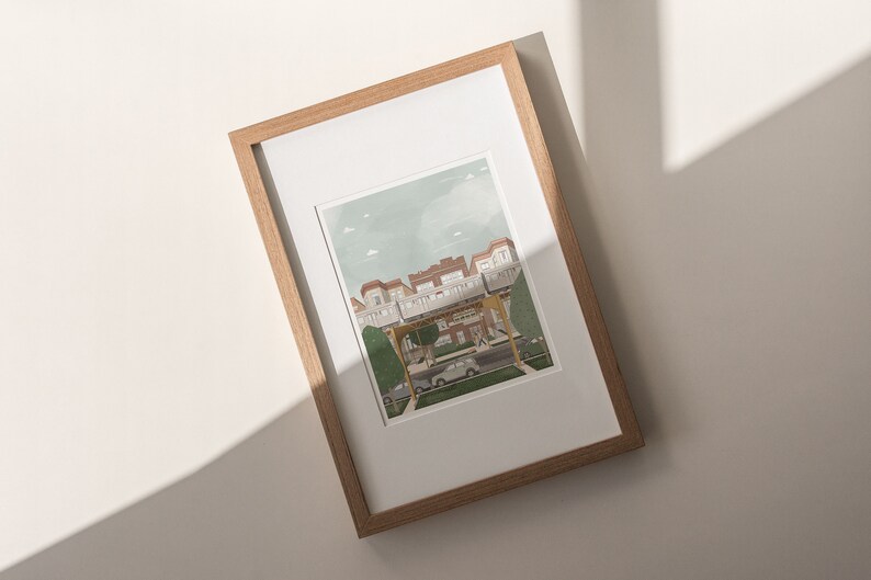 May include: A framed illustration of a street scene with a row of houses, a car, and people walking. The houses are painted in shades of brown and white, with green trees and a blue sky in the background.