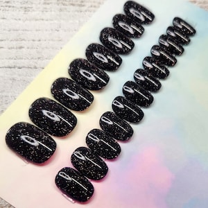 May include: A set of 10 black oval-shaped press-on nails with a sparkly finish and a white accent design.
