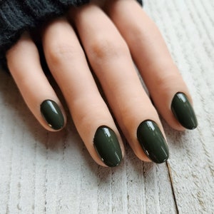May include: Close-up of a hand with four fingers painted with dark green nail polish.