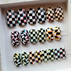 May include: Set of 15 colorful press-on nails with checkered, swirl, and abstract designs. The nails are in various shades of black, white, red, blue, yellow, and green.