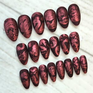 Könnte beinhalten: Set mit 20 burgunderfarbenen falschen Nägeln mit einem goldenen Drachenmuster. Die Nägel sind lang und oval.