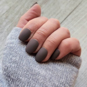 Peut inclure: Gros plan d'une main avec des ongles courts et ovales peints d'une couleur marron mate.