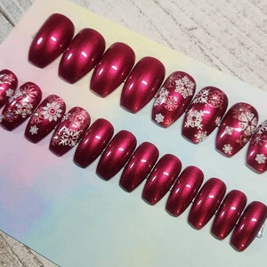May include: Set of ten burgundy coffin-shaped press-on nails with a snowflake design. The nails have a glossy finish.