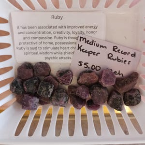 Puede incluir: Una pequeña colección de cristales de rubí rojo en una cesta de plástico blanca. Los cristales están etiquetados como "Record Rubies" y "Medium Keeper" con un precio de 5,00 €.