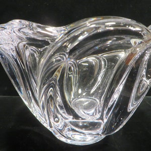 May include: A clear glass bowl with a wavy, organic design. The bowl is made of thick glass and has a smooth, polished finish.