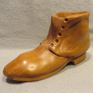 May include: A wooden boot-shaped planter with a brown finish. The boot has a lace-up design and a rounded toe.