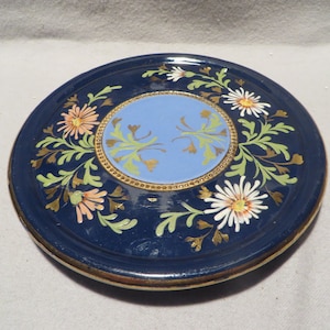 May include: A blue and white ceramic plate with a gold rim and floral design. The center of the plate features a light blue circle with gold leaf designs.