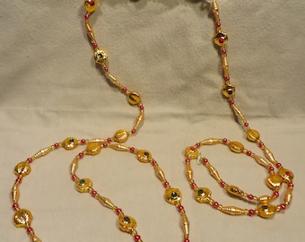 May include: A gold beaded garland with red and green accents. The beads are made of metal and have a shiny finish. The garland is perfect for decorating a Christmas tree or adding a festive touch to your home decor.