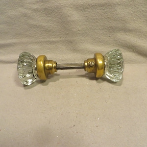 May include: A pair of antique glass door knobs with brass accents. The knobs are clear glass with a faceted design.