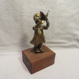 May include: A bronze sculpture of a person holding a butterfly. The sculpture is on a wooden base.