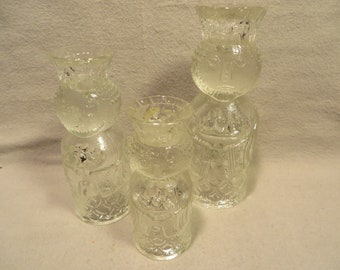 May include: Three clear glass candle holders with a textured surface and a whimsical design. The candle holders are shaped like figures with faces and bodies.