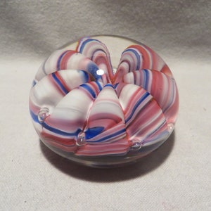 May include: A glass paperweight with a swirling pattern of pink, white, and blue. The paperweight has small air bubbles trapped inside.