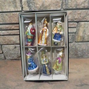 May include: Set of eight glass Christmas ornaments featuring figures in colorful robes and hats. The ornaments are packaged in a white box with a black border.