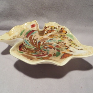 May include: A white glass bowl with a wavy edge and a colorful, abstract design. The design features swirls of brown, orange, green, and blue.