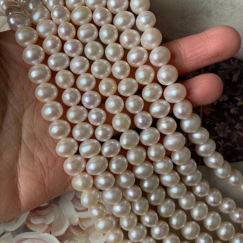 May include: A strand of white freshwater pearls, with a slight iridescent sheen. The pearls are round and smooth, and they are strung on a clear thread. The pearls are approximately 8mm in diameter.