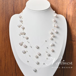 May include: A white pearl necklace with multiple strands of pearls on a clear string. The necklace is displayed on a white mannequin bust.