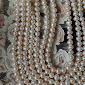 May include: A strand of white pearl beads, arranged in multiple rows, creating a luxurious and elegant look. The pearls are smooth and lustrous, with a subtle shimmer.