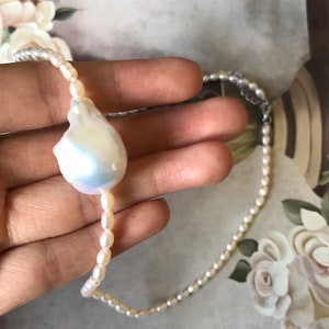 Peut inclure: Un collier de perles blanches avec un pendentif en perle irr&eacute;guli&egrave;re de grande taille. Le collier est compos&eacute; de petites perles rondes.