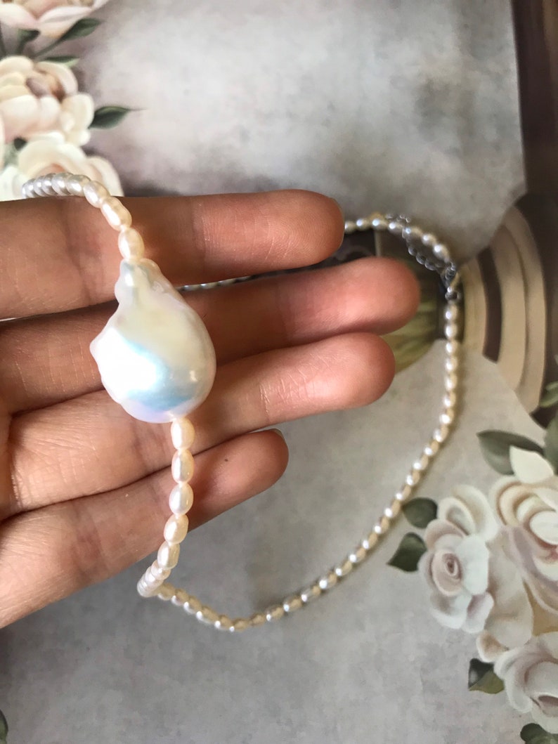 Peut inclure: Un collier de perles blanches avec un pendentif en perle irr&eacute;guli&egrave;re de grande taille. Le collier est compos&eacute; de petites perles rondes.