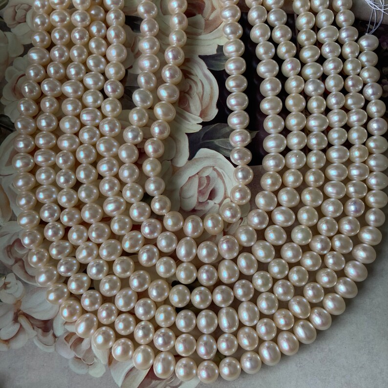 May include: A strand of white freshwater pearls, with a smooth, round shape. The pearls are strung together on a clear thread, and they are arranged in a loose, flowing pattern.