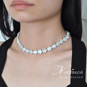 May include: A white pearl choker necklace with star-shaped pearls. The necklace is on a model wearing a black top.