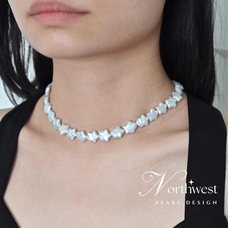 May include: A white pearl choker necklace with star-shaped pearls. The necklace is on a model wearing a black top.