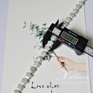 May include: A strand of white star-shaped freshwater pearls, measured with a caliper showing a size of 11.7 mm. The pearls are strung on a white thread and are arranged in a straight line. The image also includes a sprig of green leaves and the text "Love what" and "Northwest Pearl Design".