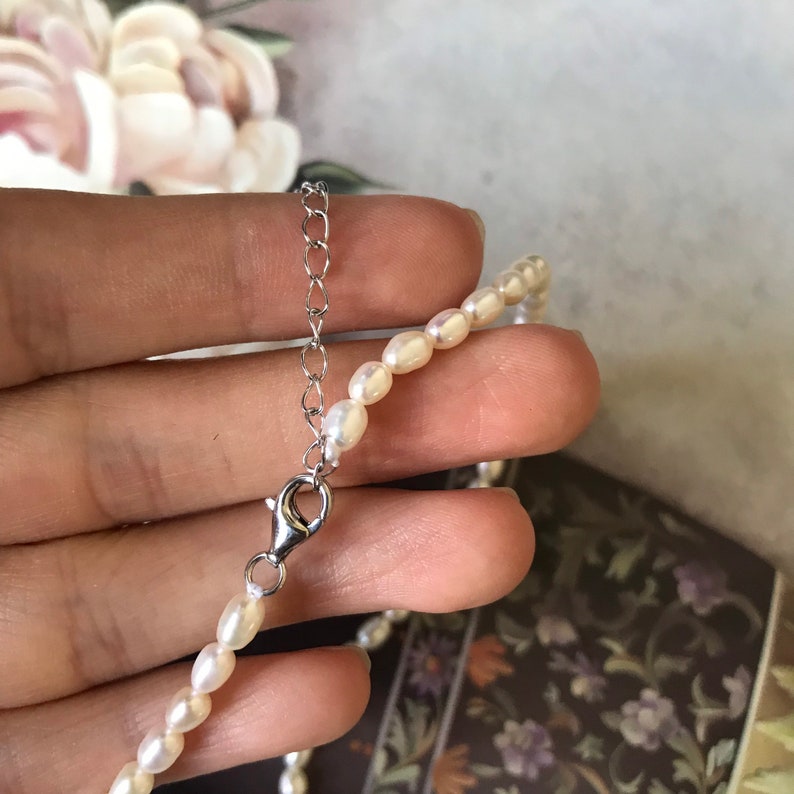 Peut inclure: Un collier d&eacute;licat de perles avec un fermoir argent&eacute;. Le collier est compos&eacute; de petites perles blanches et mesure environ 40 cm de long.