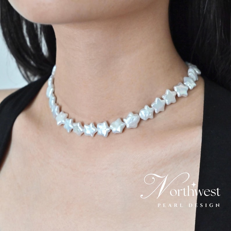 May include: A white pearl necklace with star-shaped pearls. The necklace is on a model wearing a black top. The necklace is a choker style and sits close to the neck.