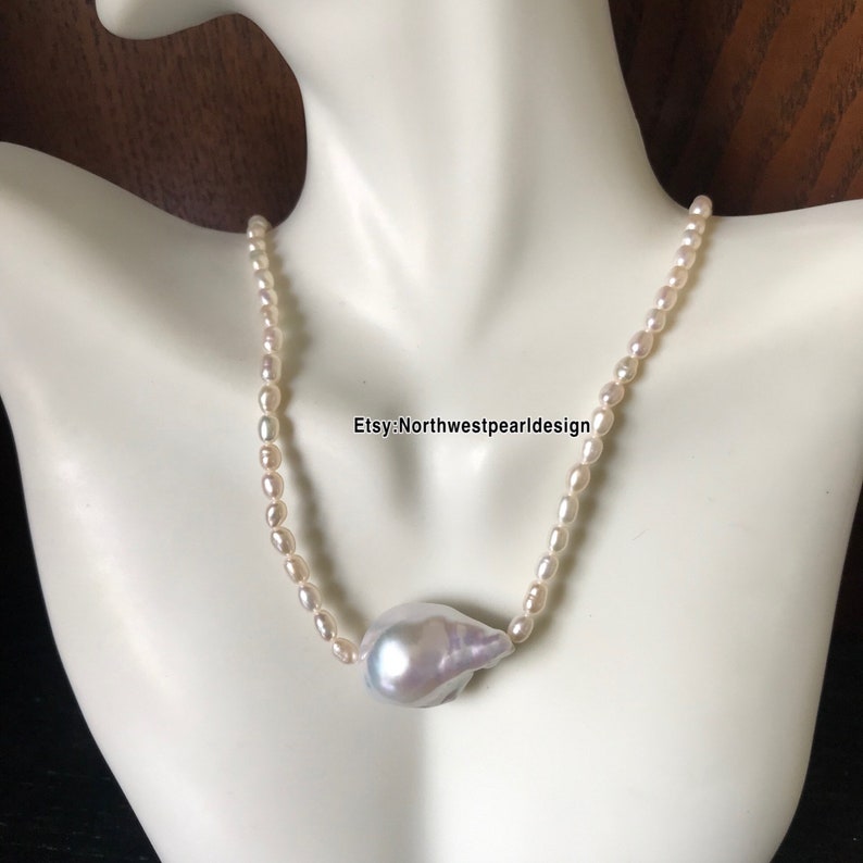 Peut inclure: Un collier de perles blanches avec un grand pendentif baroque en perle iridescente blanc cass&eacute;. Le collier est sur un mannequin blanc.
