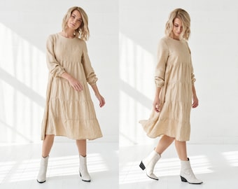 May include: A beige tiered linen dress with long sleeves and a round neckline. The dress is worn with white cowboy boots.