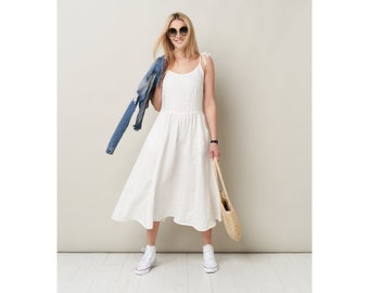 Op de afbeelding: Een witte, mouwloze midi-jurk met een geplooide rok en dunne bandjes. Het model draagt witte sneakers en een zonnebril.