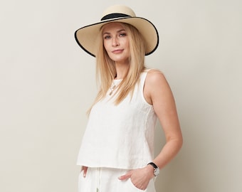 Puede incluir: Una mujer con un top blanco de lino y pantalones a juego con un sombrero de paja de ala ancha con una banda negra.
