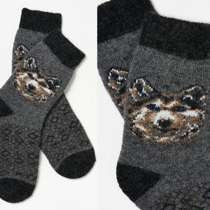 May include: A pair of grey wool socks with a black and white geometric pattern. The socks feature a wolf face design in the centre.