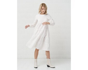 May include: A white tiered linen dress with long sleeves and a round neckline. The dress is midi length and has a relaxed fit.