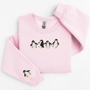 Pu&ograve; includere: Una felpa rosa chiaro con girocollo e maniche lunghe. La parte anteriore presenta un disegno ricamato di quattro pinguini. Un pinguino &egrave; ricamato sulla manica sinistra. I pinguini sono neri, bianchi e gialli.