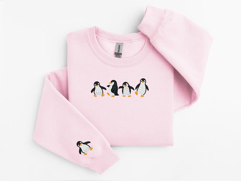 Pu&ograve; includere: Una felpa rosa chiaro con girocollo e maniche lunghe. La parte anteriore presenta un disegno ricamato di quattro pinguini. Un pinguino &egrave; ricamato sulla manica sinistra. I pinguini sono neri, bianchi e gialli.
