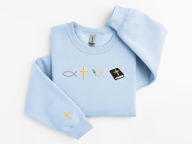 May include: A light blue sweatshirt with a Christian symbol design. The symbols include a fish, a cross, an olive branch, a dove, and a closed book with a cross on the cover.